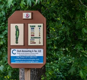 A golf course hole 8 sign at Spring Lake Country Club stands among green trees, displaying yardages, par info, and a hole map. Below it is an ad for Clark Accounting & Tax, LLC, with contact details in blue and white.