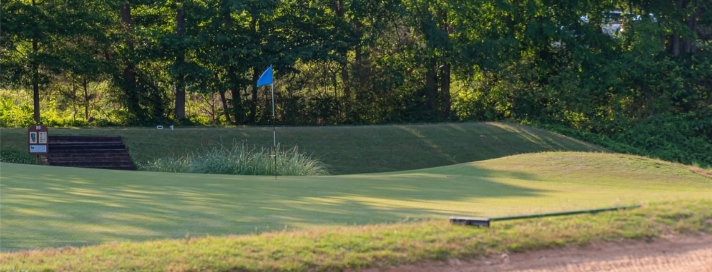A golf green at Spring Lake Country Club with a flag marking the hole, surrounded by lush grass and trees in the background on a sunny day.